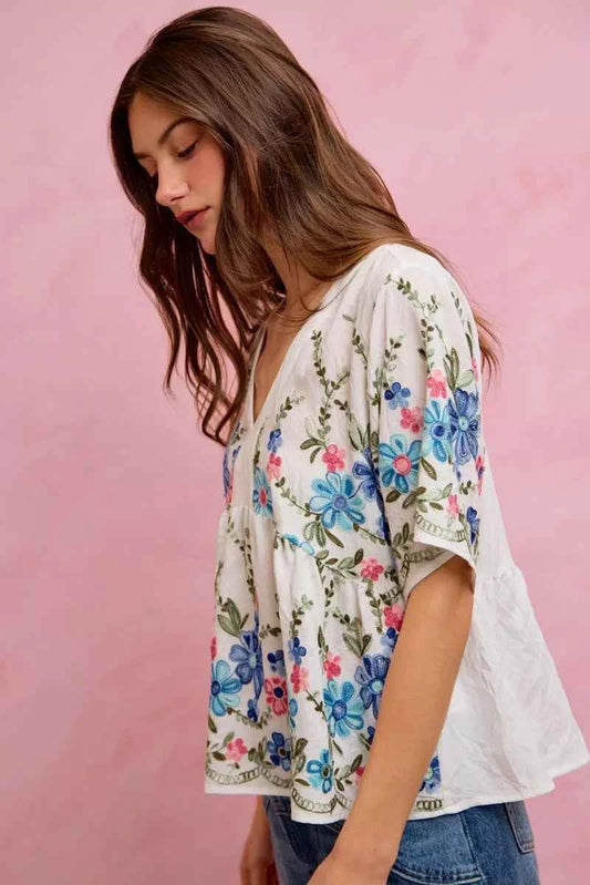 Woman wearing SO ME off white floral embroidered babydoll blouse top featuring colorful floral embroidery, flowy silhouette, short sleeves, and feminine everyday style. Side View