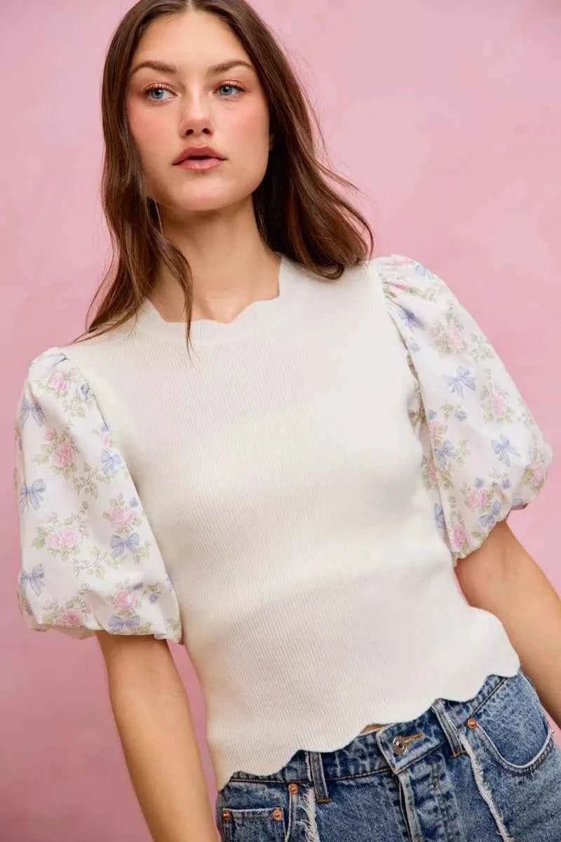 Woman wearing SO ME white floral contrast sleeve scallop sweater top featuring puff sleeves, lightweight knit fabric, feminine floral print, and scalloped trim detail. Front View
