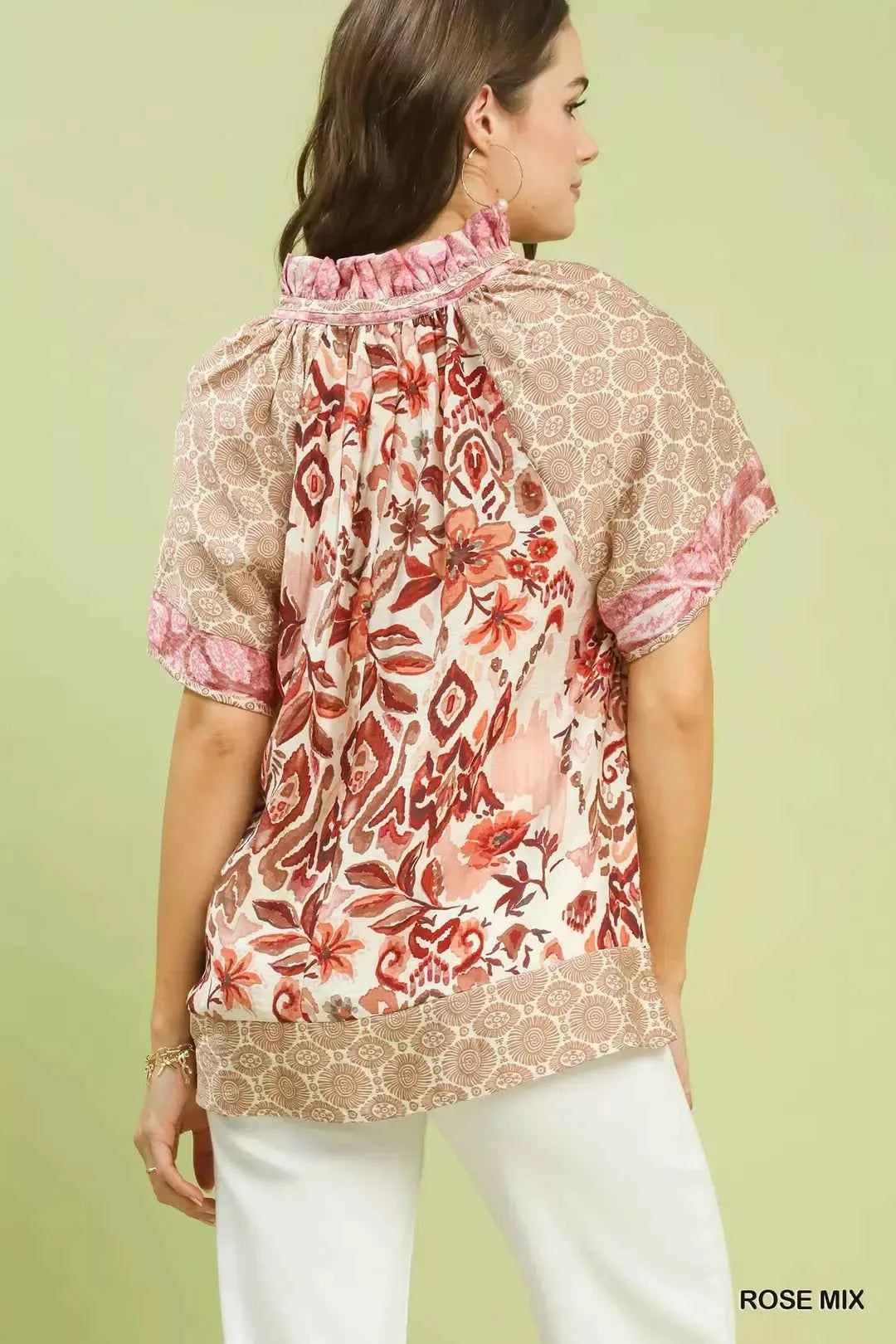 Woman wearing Umgee Rose Mix boho floral patchwork blouse with V-neckline and short sleeves paired with white pants. Back View