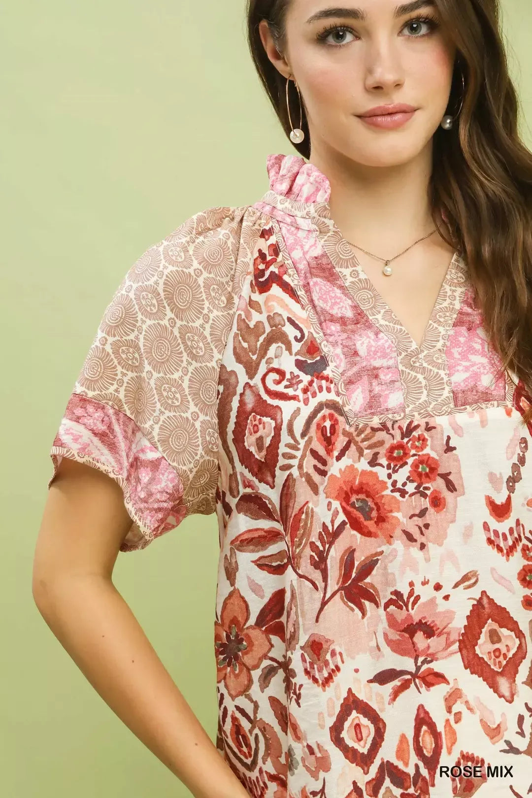Woman wearing Umgee Rose Mix boho floral patchwork blouse with V-neckline and short sleeves paired with white pants. Close View
