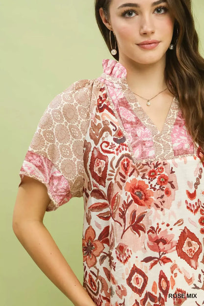Woman wearing Umgee Rose Mix boho floral patchwork blouse with V-neckline and short sleeves paired with white pants. Close View