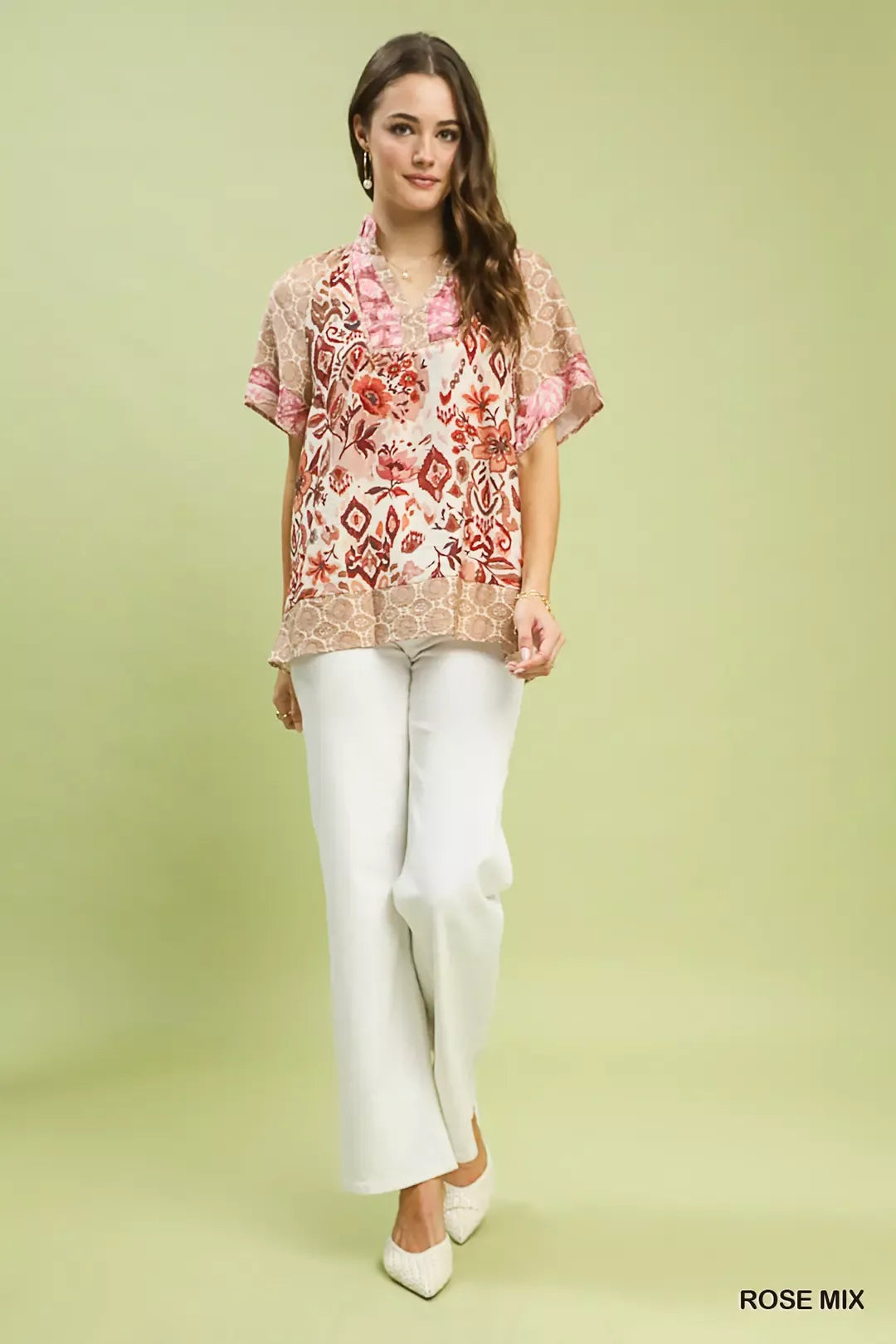 Woman wearing Umgee Rose Mix boho floral patchwork blouse with V-neckline and short sleeves paired with white pants. Full View