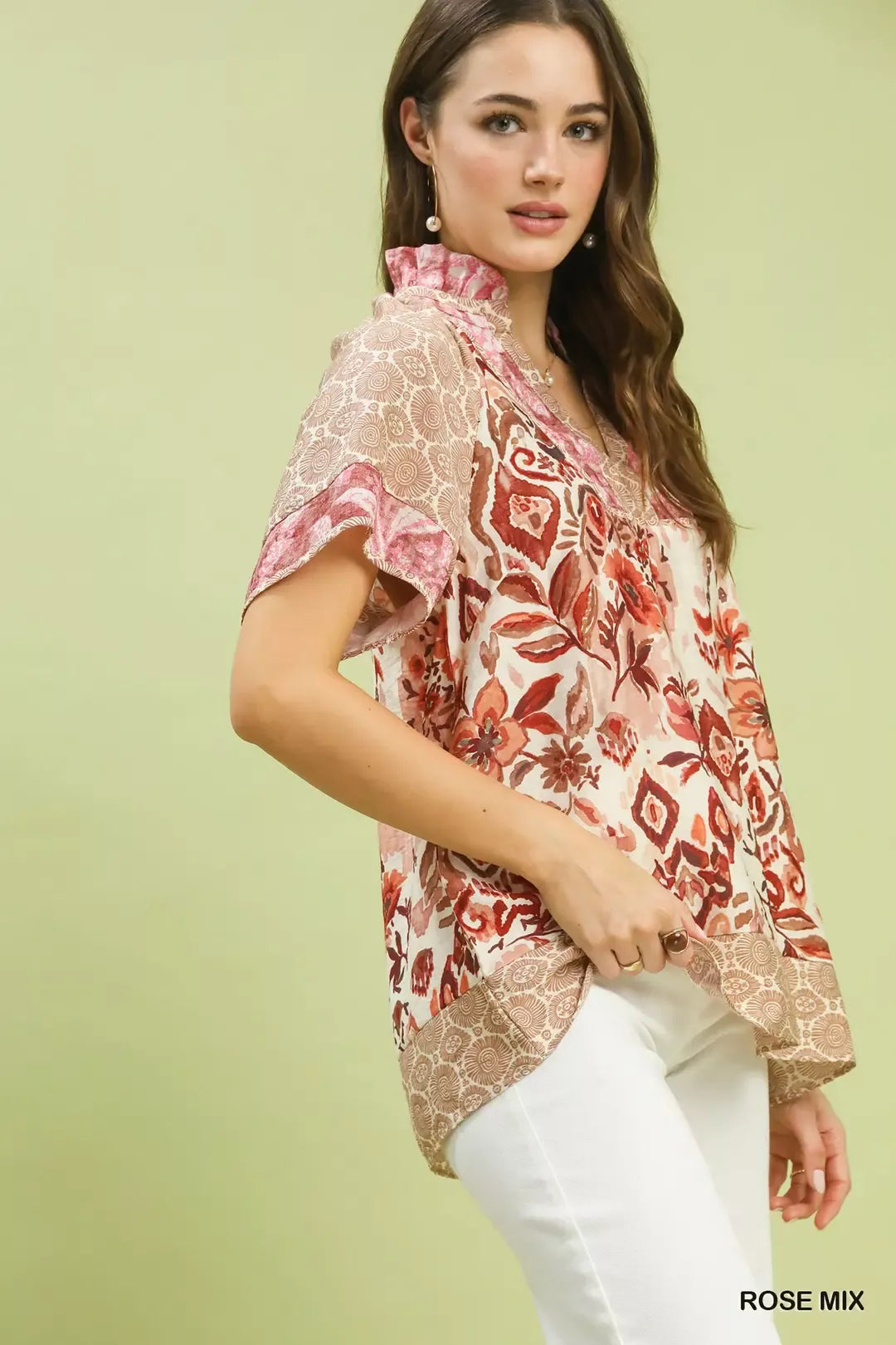 Woman wearing Umgee Rose Mix boho floral patchwork blouse with V-neckline and short sleeves paired with white pants. Side View