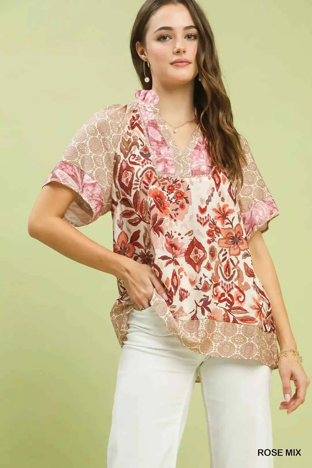 Woman wearing Umgee Rose Mix boho floral patchwork blouse with V-neckline and short sleeves paired with white pants. Front View