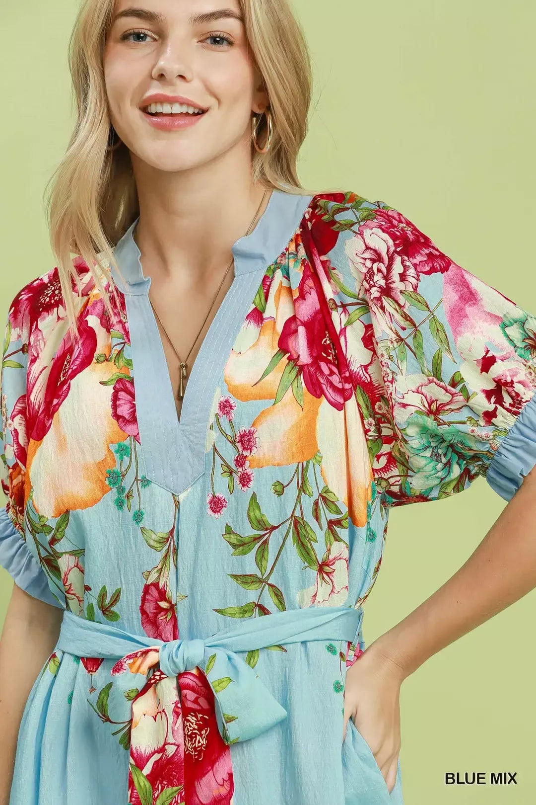 Woman wearing Umgee blue mix floral border print midi dress with split neckline, self-tie waist belt, short sleeves, and pockets. Close View