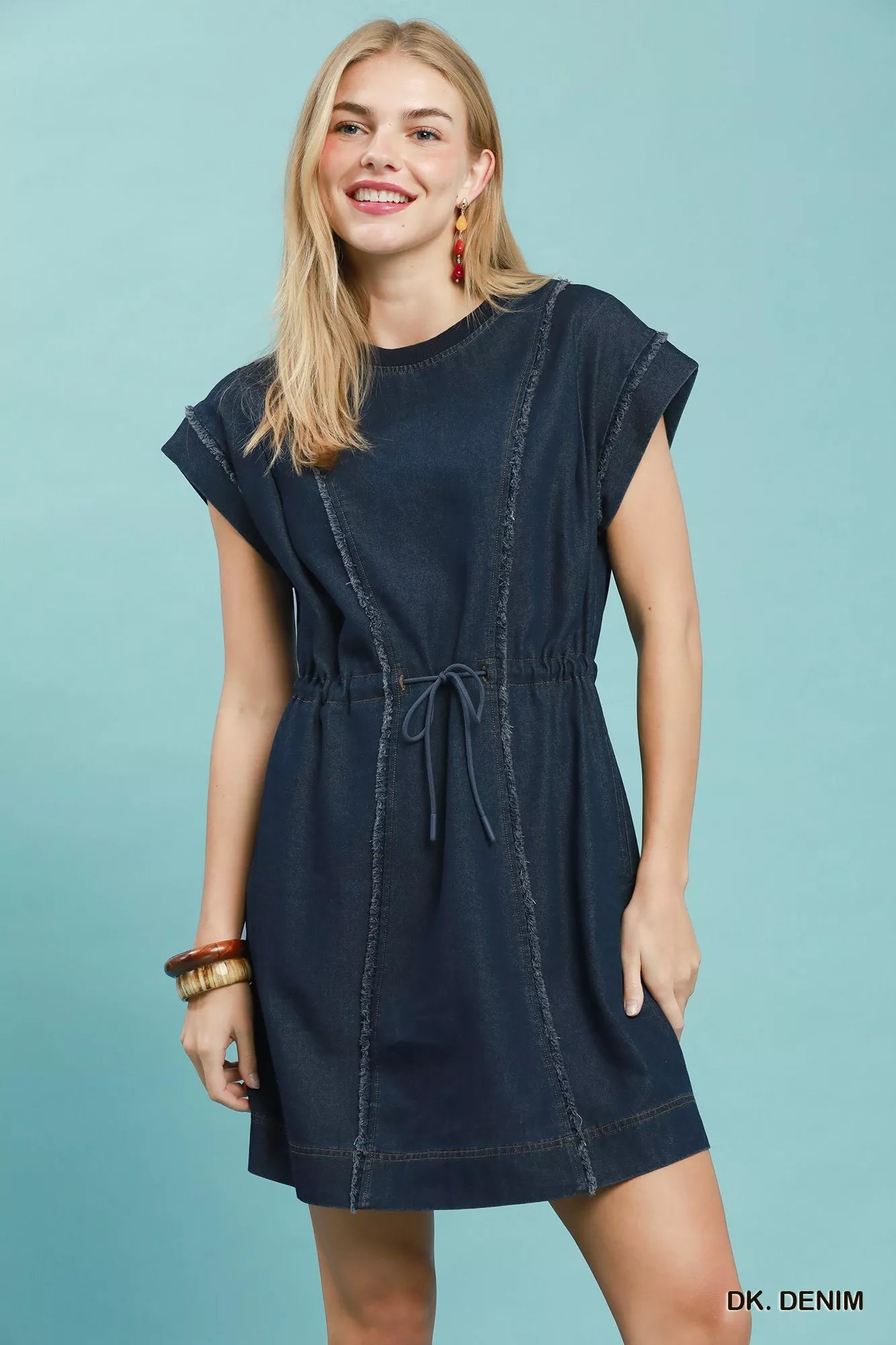Woman wearing Umgee dark denim mini dress with raw edge seam detailing, drawstring waist, cap sleeves, and side pockets. Front View