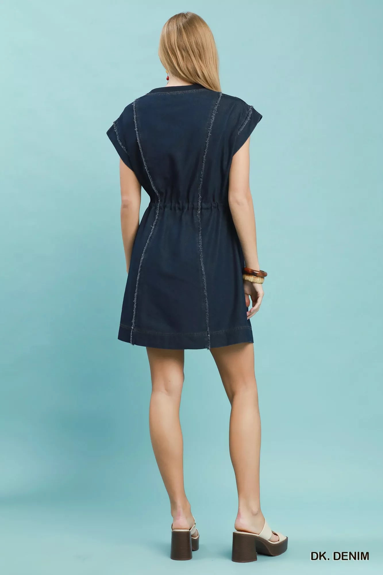 Woman wearing Umgee dark denim mini dress with raw edge seam detailing, drawstring waist, cap sleeves, and side pockets. Full Back View