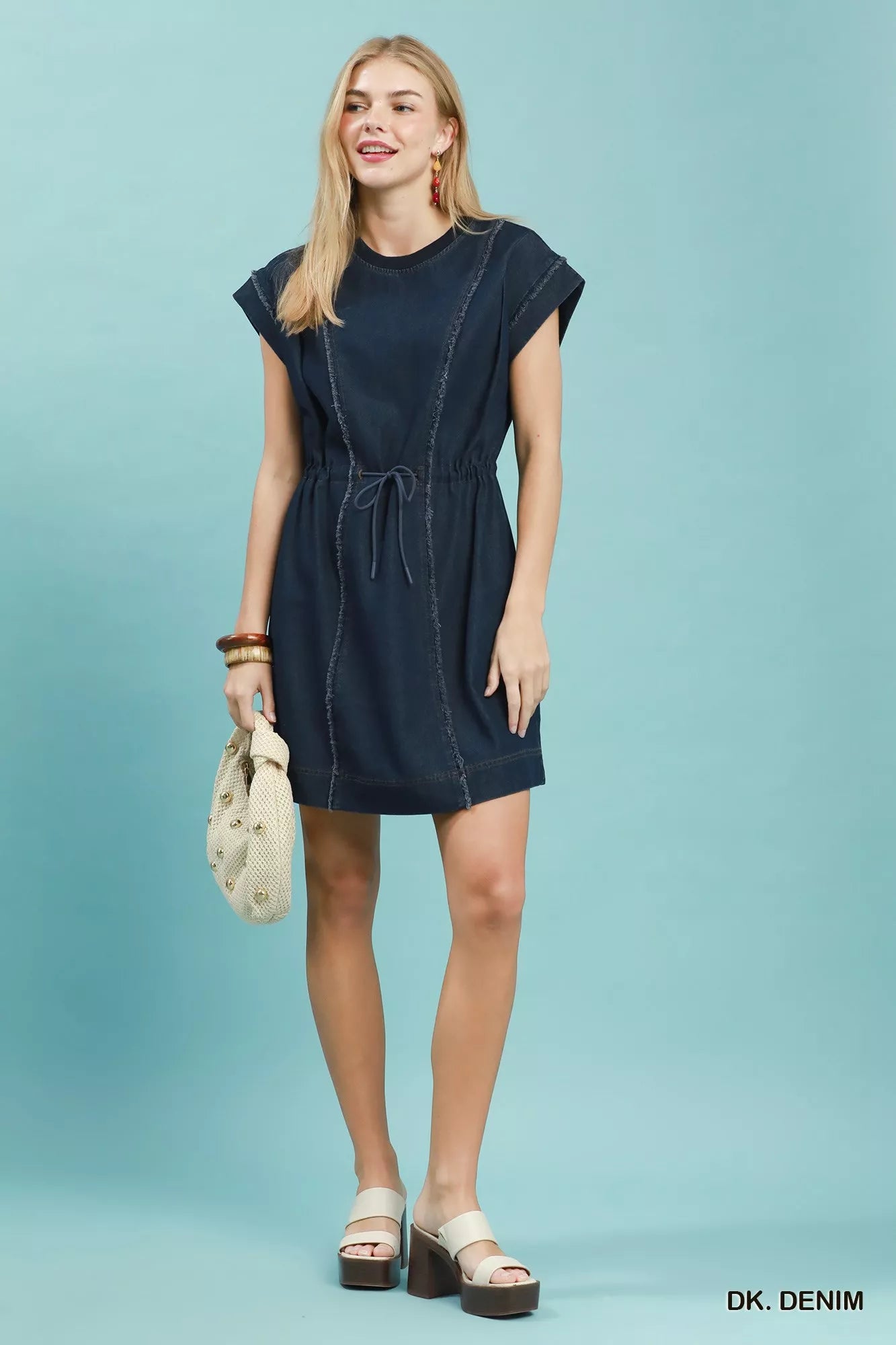 Woman wearing Umgee dark denim mini dress with raw edge seam detailing, drawstring waist, cap sleeves, and side pockets. Full View