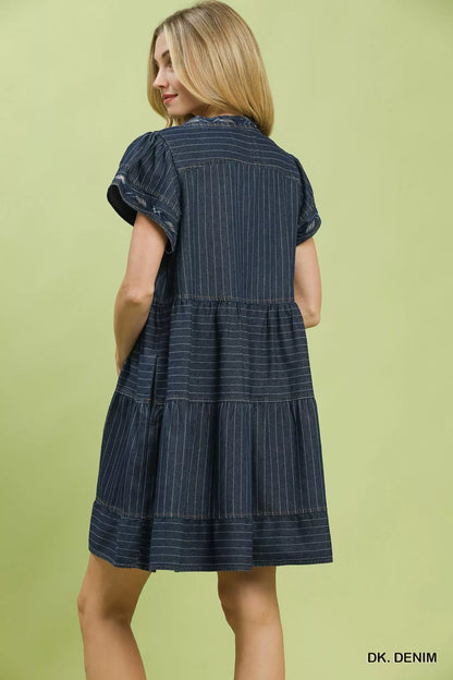 Woman wearing Umgee dark denim pinstripe tiered babydoll dress with flutter sleeves, split neckline, pockets, and relaxed flowy silhouette. Back View