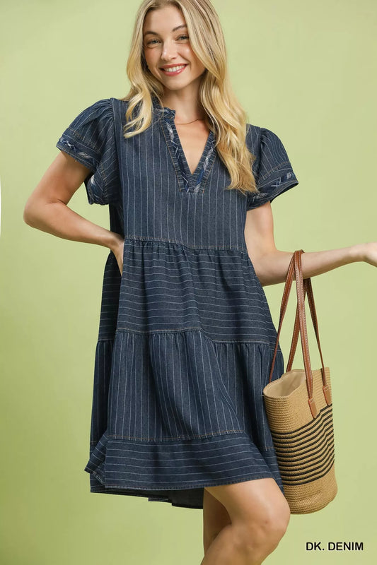 Woman wearing Umgee dark denim pinstripe tiered babydoll dress with flutter sleeves, split neckline, pockets, and relaxed flowy silhouette. Front View