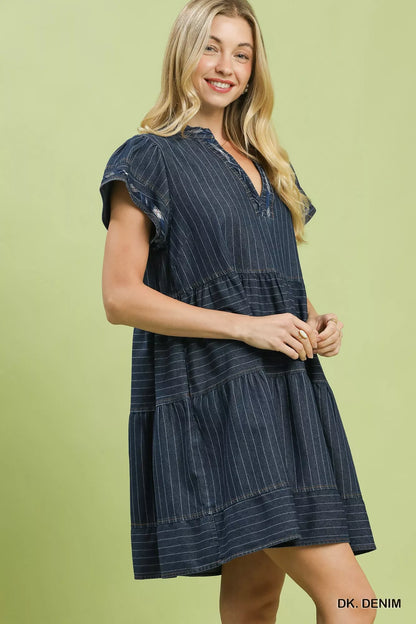 Woman wearing Umgee dark denim pinstripe tiered babydoll dress with flutter sleeves, split neckline, pockets, and relaxed flowy silhouette. Side View