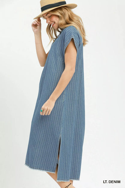 Woman wearing Umgee light denim pinstripe midi dress with collared split neckline, cap sleeves, side pockets, side slits, and raw hem detail. Side View