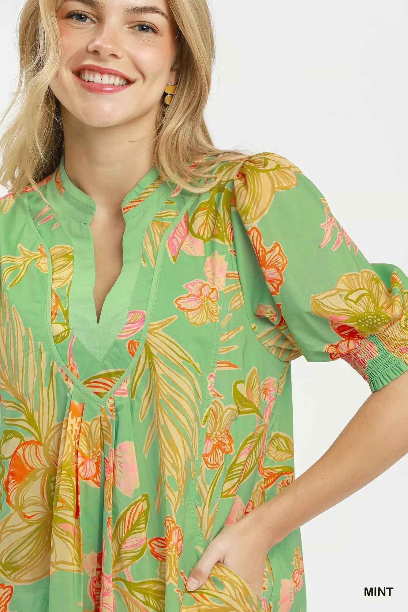 Woman wearing Umgee mint tropical floral dress with smocked sleeves, split V-neck, pockets, and flowy silhouette perfect for summer vacations and brunch. Close View