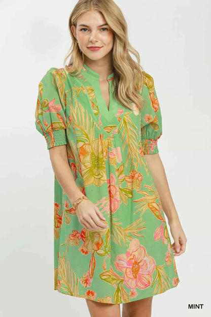 Woman wearing Umgee mint tropical floral dress with smocked sleeves, split V-neck, pockets, and flowy silhouette perfect for summer vacations and brunch. Front View