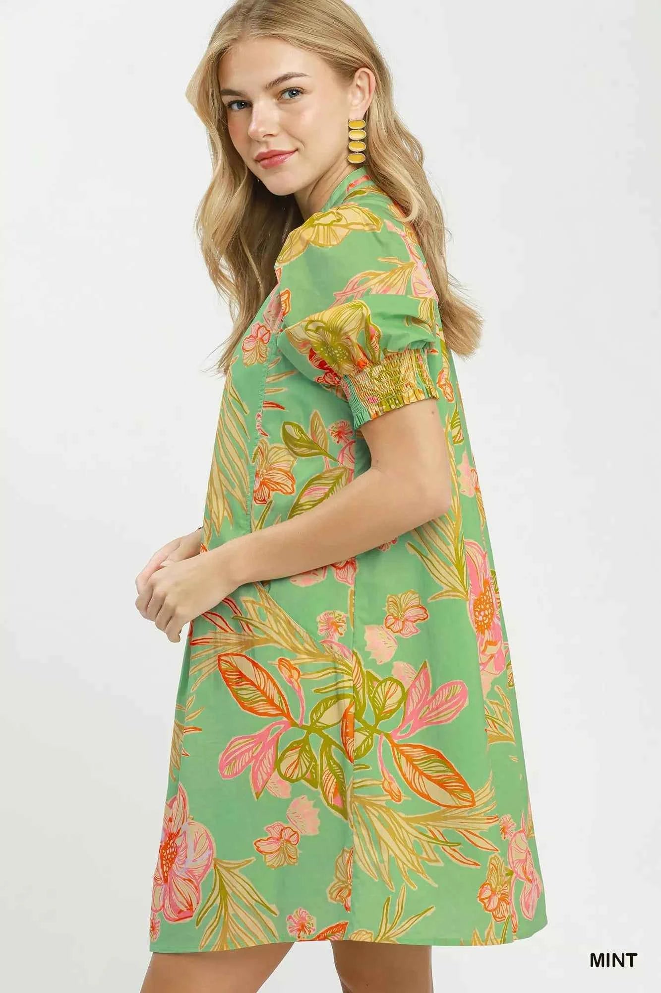 Woman wearing Umgee mint tropical floral dress with smocked sleeves, split V-neck, pockets, and flowy silhouette perfect for summer vacations and brunch. Side View
