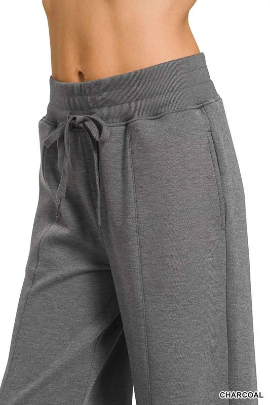 Woman wearing a Zenana charcoal scuba knit two-piece set featuring a collared short-sleeve pullover top and matching wide-leg pants with pockets. Side View with Drawstring