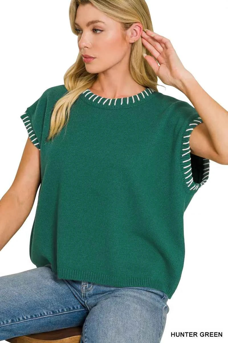 Woman wearing a Zenana hunter green oversized knit sweater vest with white contrast stitch detailing, cap sleeves, and a relaxed fit styled with denim jeans.