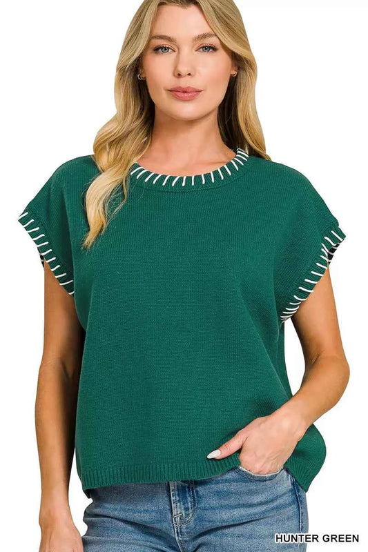 Woman wearing a Zenana hunter green oversized knit sweater vest with white contrast stitch detailing, cap sleeves, and a relaxed fit styled with denim jeans. Front View