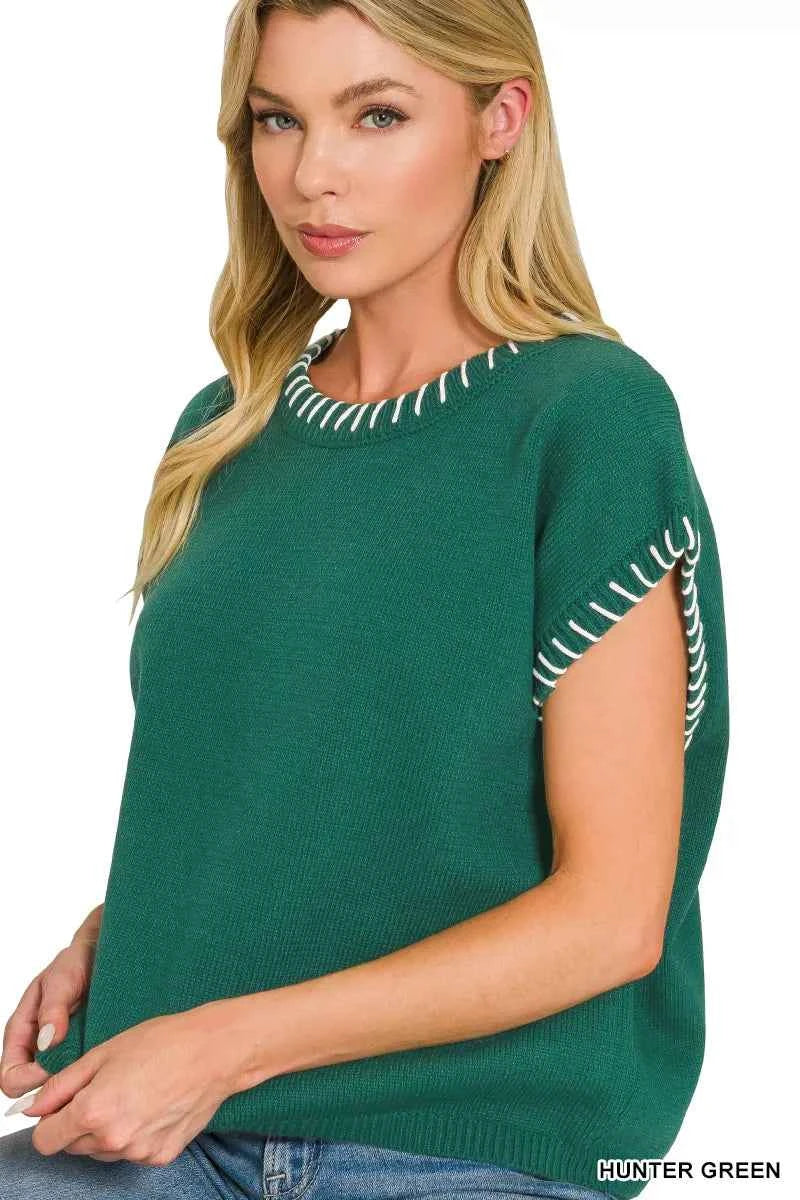 Woman wearing a Zenana hunter green oversized knit sweater vest with white contrast stitch detailing, cap sleeves, and a relaxed fit styled with denim jeans. Side View