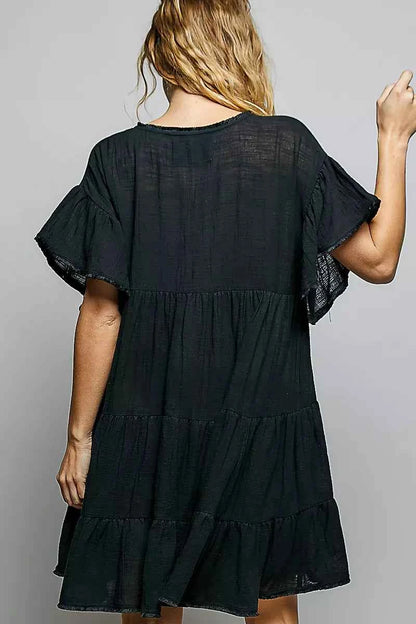 Woman wearing a black POL cotton dress featuring a V-neckline, tiered ruffle design, and relaxed flowy silhouette.
 Back View