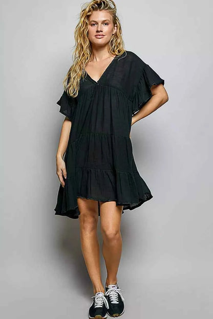 Woman wearing a black POL cotton dress featuring a V-neckline, tiered ruffle design, and relaxed flowy silhouette.
 Front full view