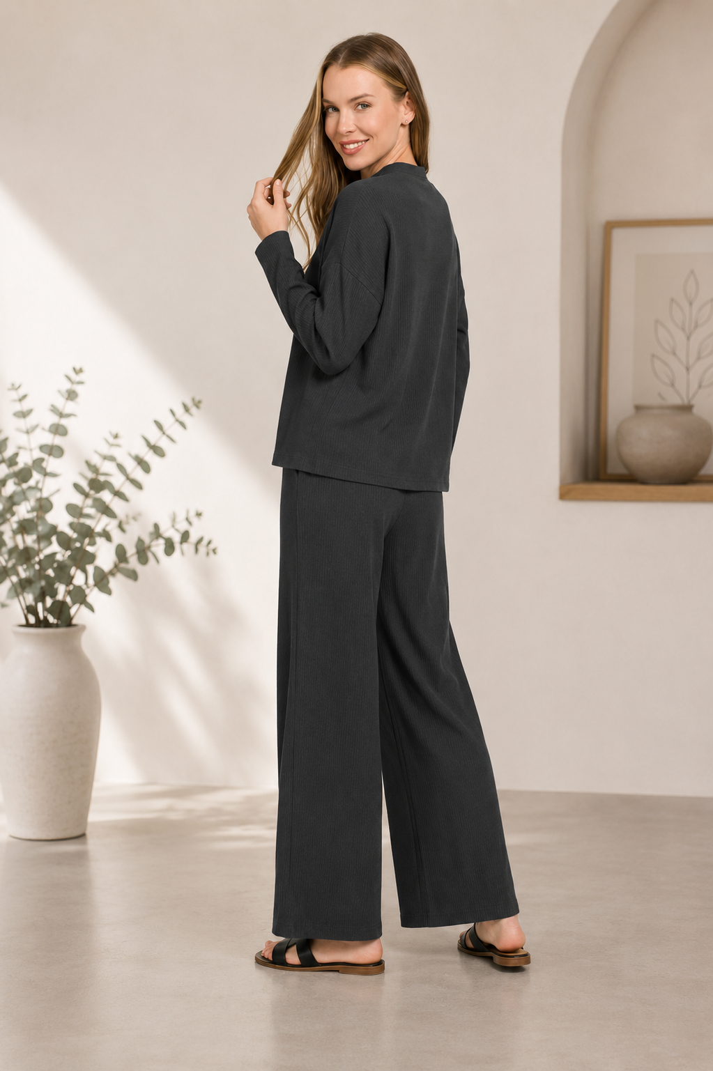 Woman wearing a black ribbed viscose long sleeve sweater with matching high-waisted wide leg pants by Zenana. back view
