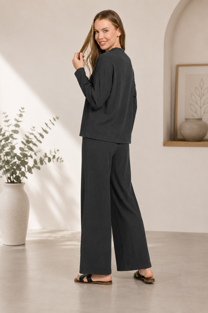 Woman wearing a black ribbed viscose long sleeve sweater with matching high-waisted wide leg pants by Zenana. back view