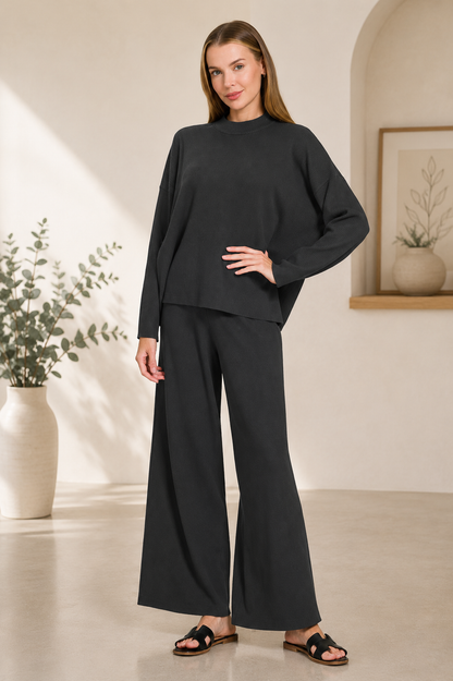 Woman wearing a black ribbed viscose long sleeve sweater with matching high-waisted wide leg pants by Zenana. front view 2