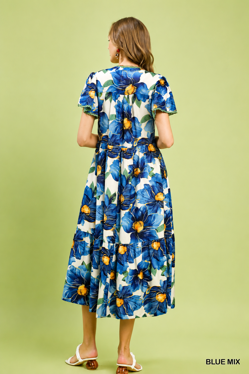 Woman wearing a blue tropical floral tiered midi dress by Umgee featuring flutter sleeves, lace trim, a V-neckline, hidden pockets, and a flowing silhouette. Back View