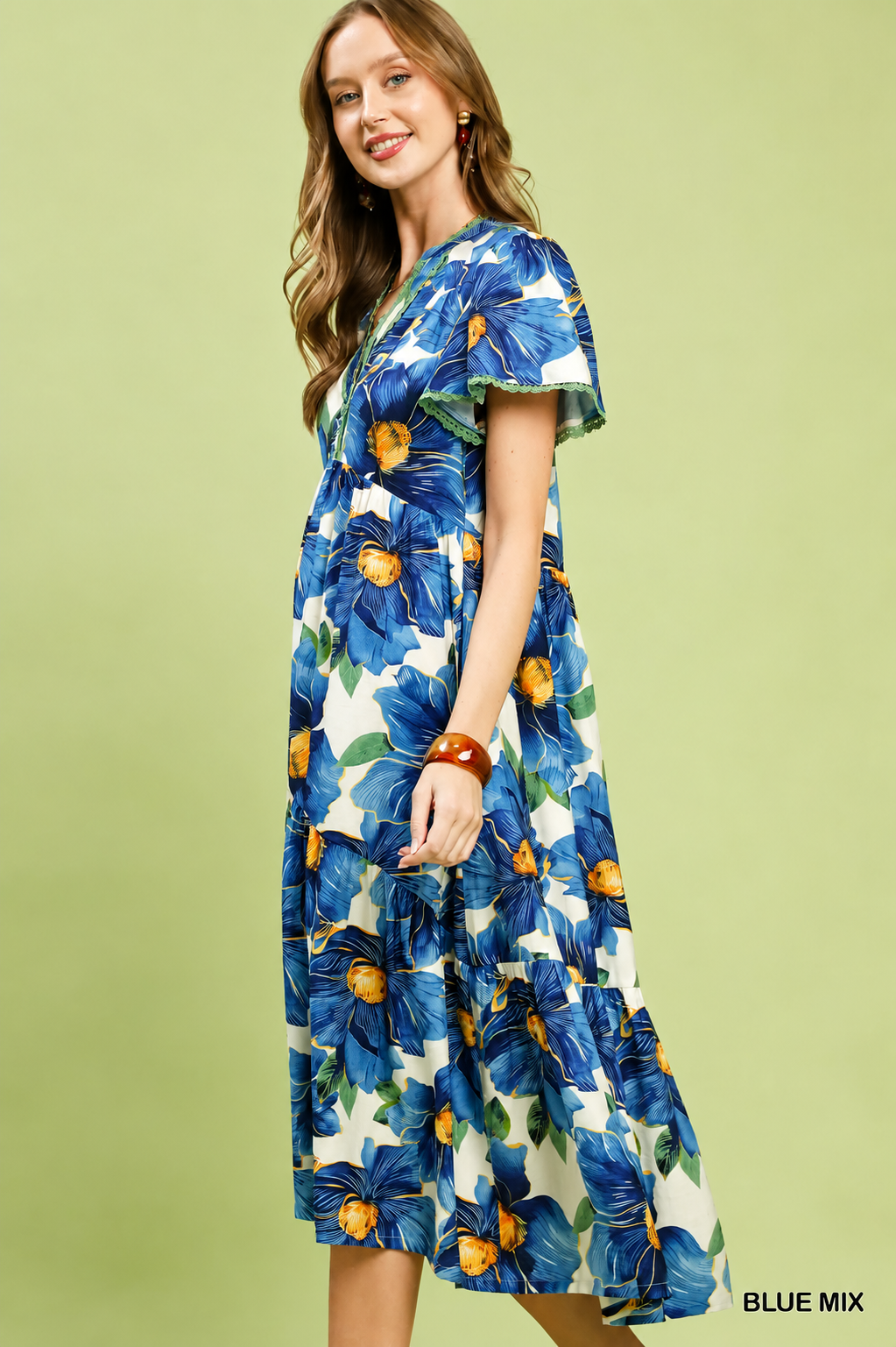 Woman wearing a blue tropical floral tiered midi dress by Umgee featuring flutter sleeves, lace trim, a V-neckline, hidden pockets, and a flowing silhouette. Side View