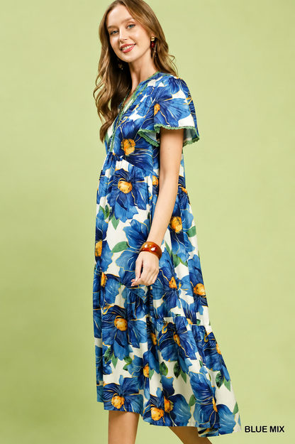 Woman wearing a blue tropical floral tiered midi dress by Umgee featuring flutter sleeves, lace trim, a V-neckline, hidden pockets, and a flowing silhouette. Side View