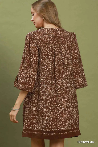 Woman wearing a brown geometric print tunic dress with a V-neckline, tassel ties, and three-quarter slit sleeves by Umgee. Back View