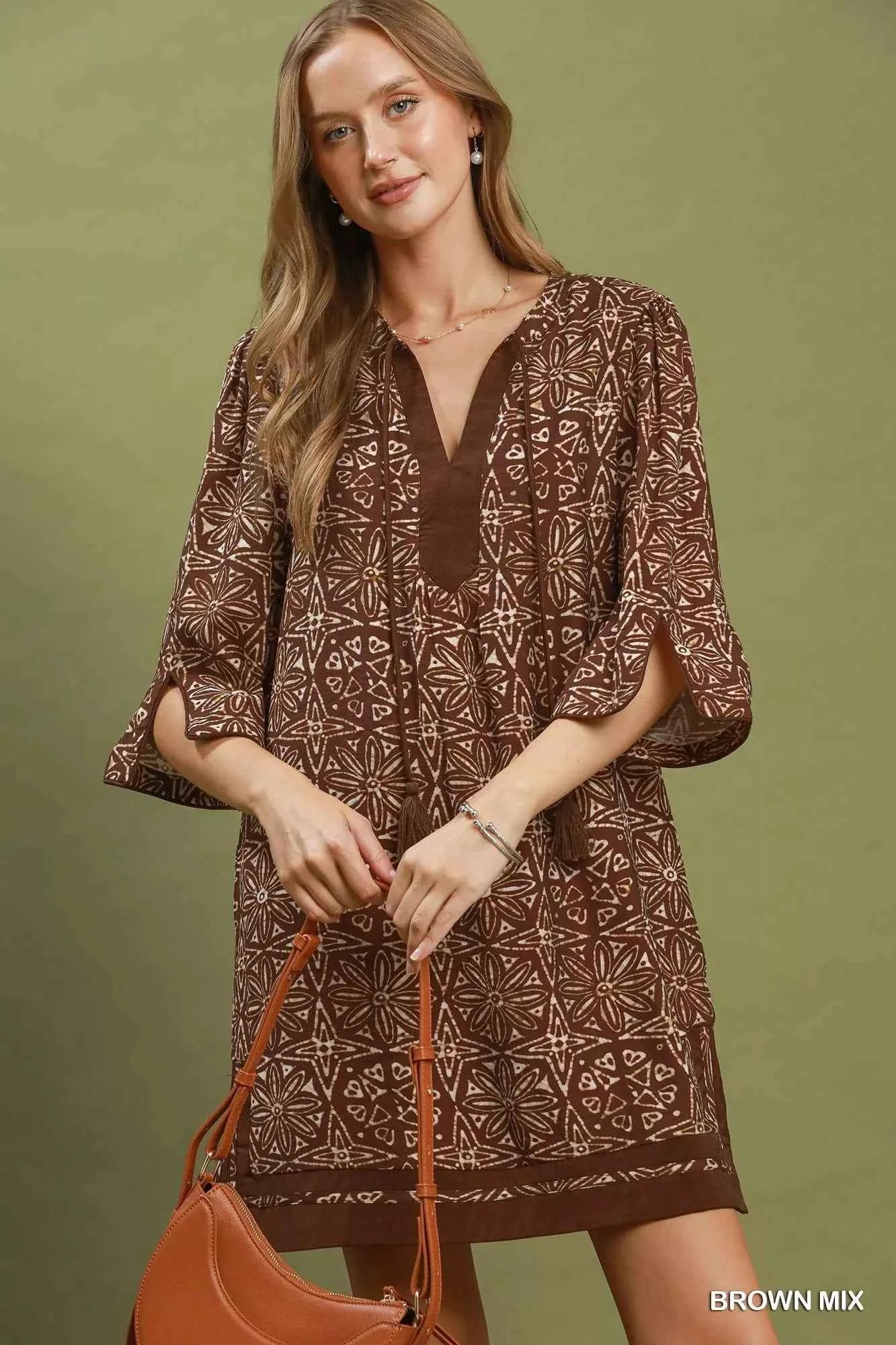 Woman wearing a brown geometric print tunic dress with a V-neckline, tassel ties, and three-quarter slit sleeves by Umgee. Front View 2