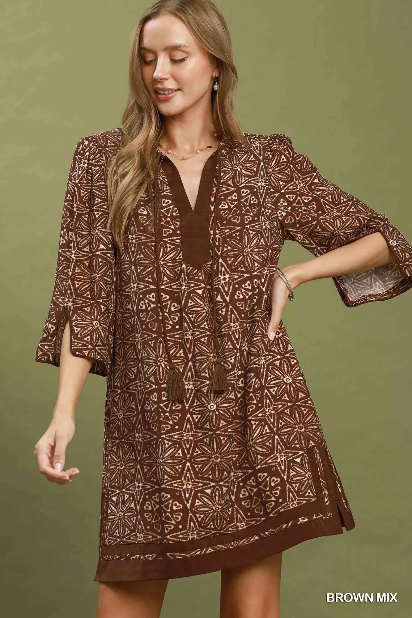 Woman wearing a brown geometric print tunic dress with a V-neckline, tassel ties, and three-quarter slit sleeves by Umgee. Front view