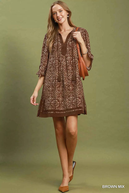 Woman wearing a brown geometric print tunic dress with a V-neckline, tassel ties, and three-quarter slit sleeves by Umgee. full view