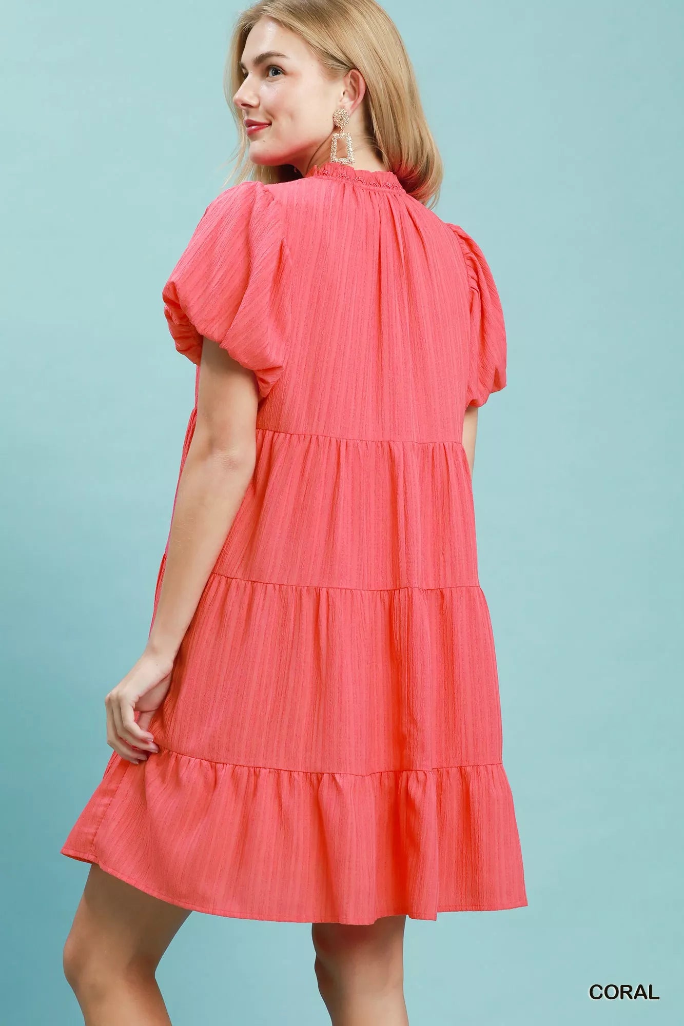 Woman wearing a coral tiered babydoll mini dress with puff sleeves and pockets by Umgee Back View