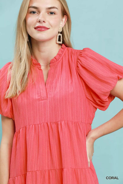 Woman wearing a coral tiered babydoll mini dress with puff sleeves and pockets by Umgee Close View