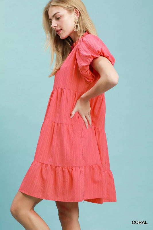 Woman wearing a coral tiered babydoll mini dress with puff sleeves and pockets by Umgee Side View