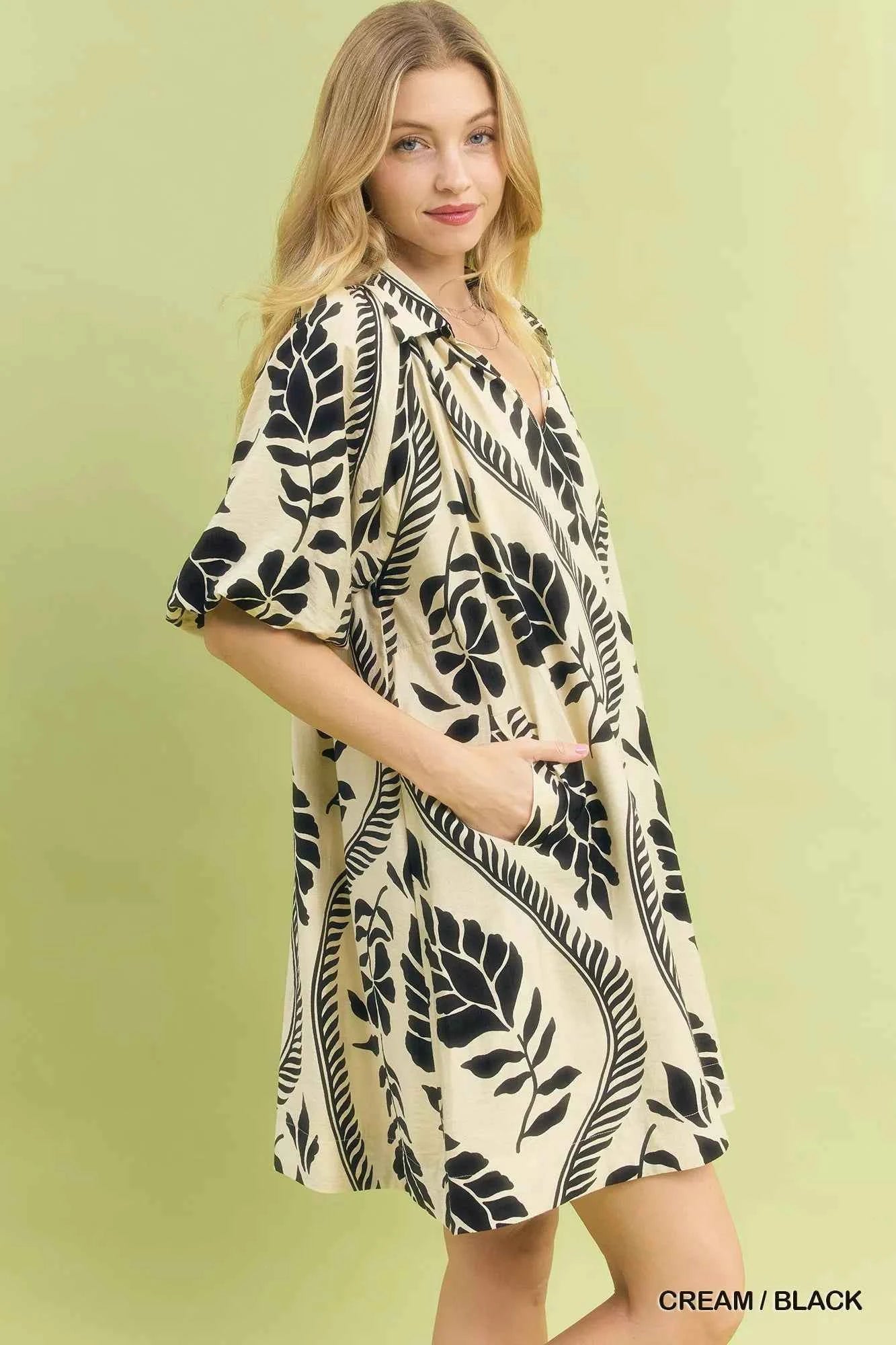 Woman wearing a cream and black leafy ogee print mini dress with a collared V-neckline and side pockets by Umgee. Side View