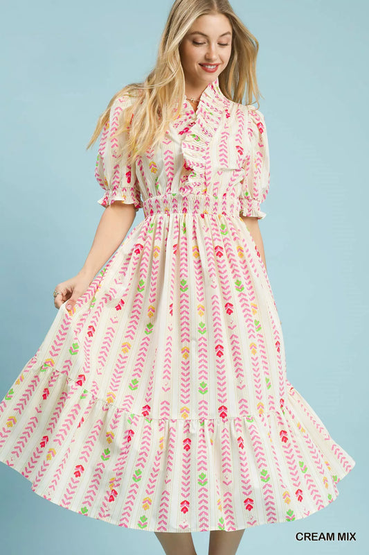 Woman wearing a cream floral print midi dress by Umgee featuring a smocked waist, tie neckline, puff sleeves, tiered skirt, and colorful spring-inspired pattern. Front view