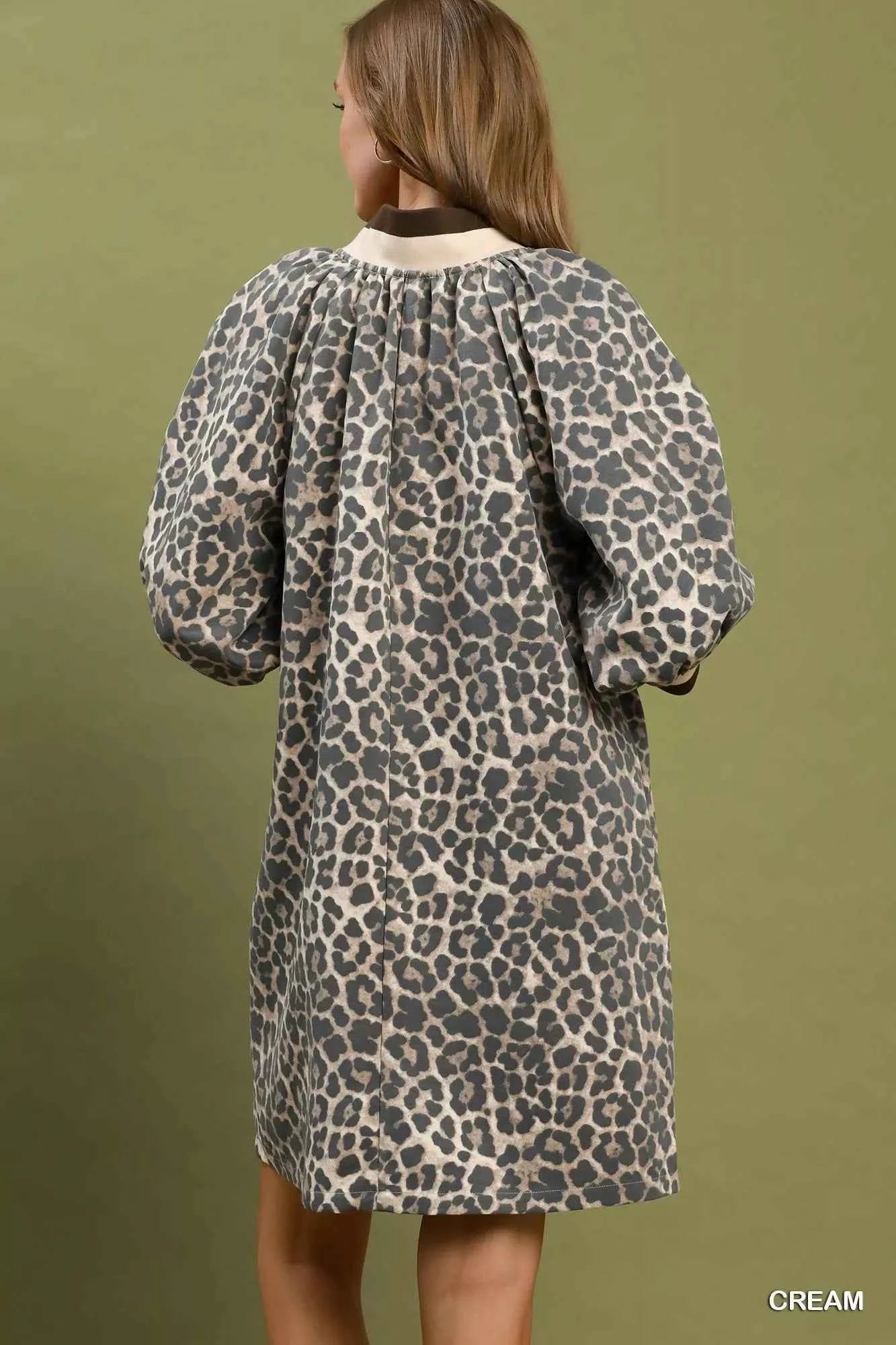 Woman wearing a cream leopard print mini dress by Umgee featuring a quarter-zip neckline, puff sleeves, contrast trim, relaxed fit, and side pockets. back view