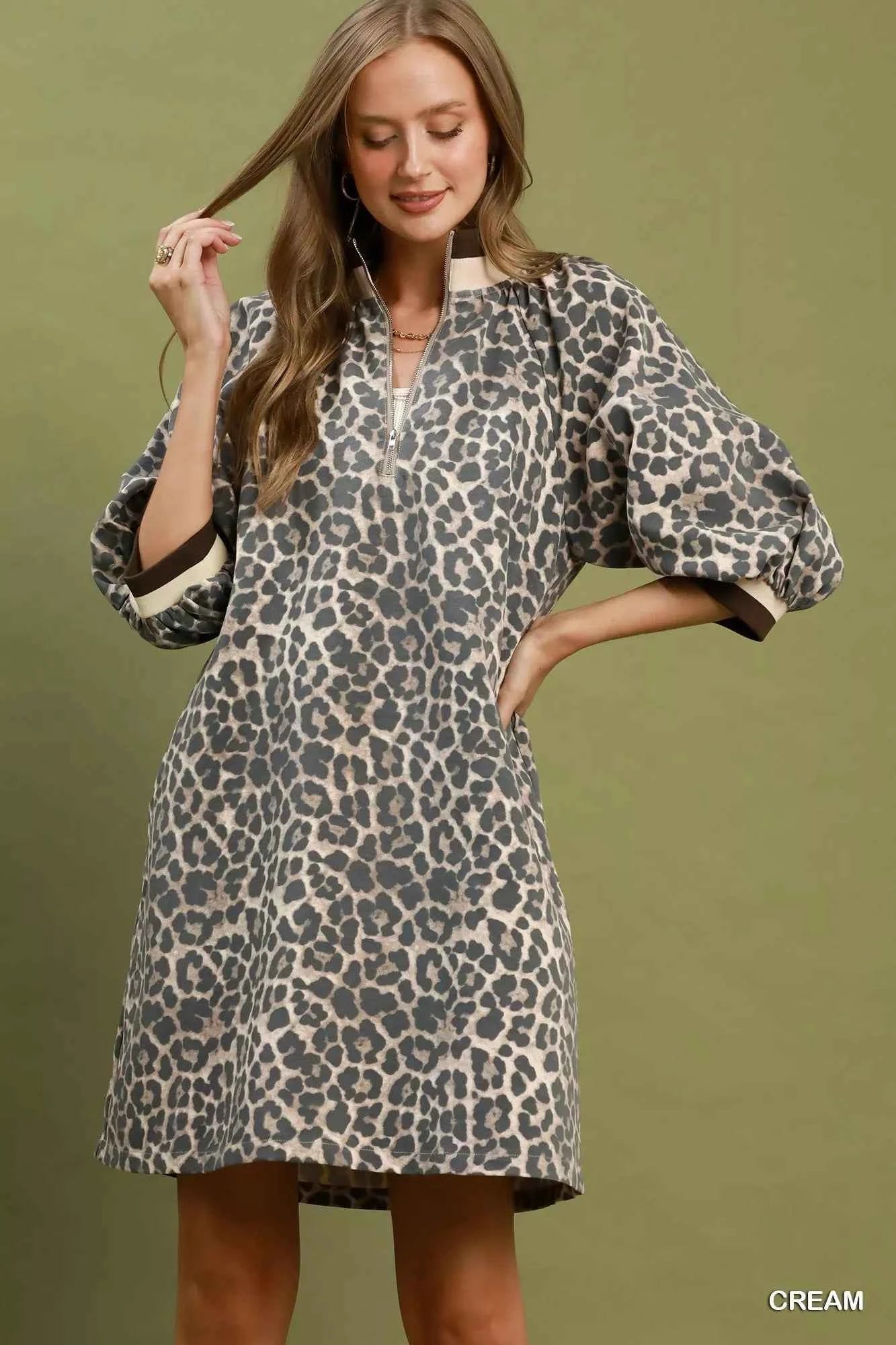 Woman wearing a cream leopard print mini dress by Umgee featuring a quarter-zip neckline, puff sleeves, contrast trim, relaxed fit, and side pockets. front view