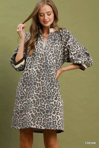 Woman wearing a cream leopard print mini dress by Umgee featuring a quarter-zip neckline, puff sleeves, contrast trim, relaxed fit, and side pockets. front view