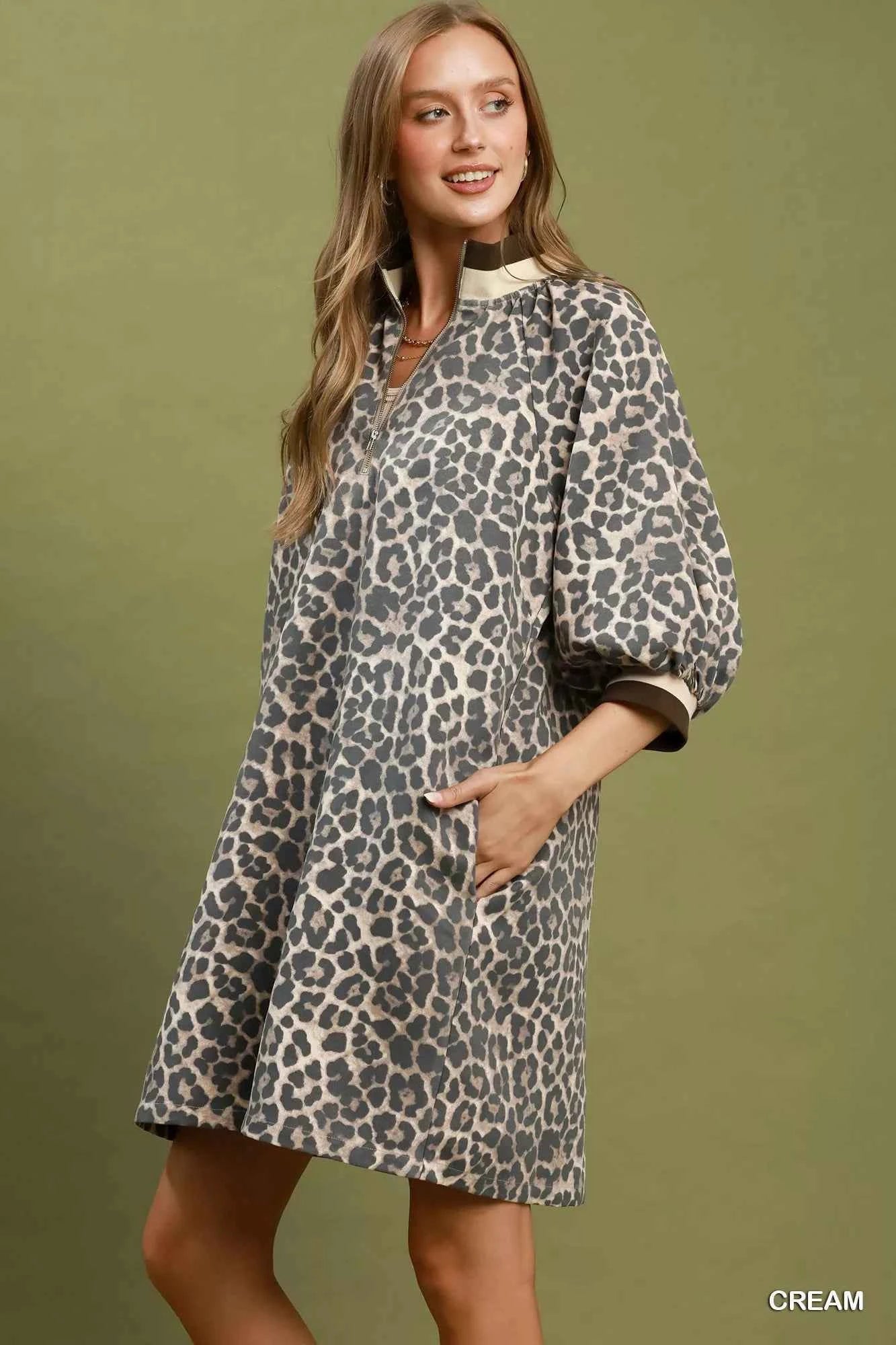Woman wearing a cream leopard print mini dress by Umgee featuring a quarter-zip neckline, puff sleeves, contrast trim, relaxed fit, and side pockets. pocket view