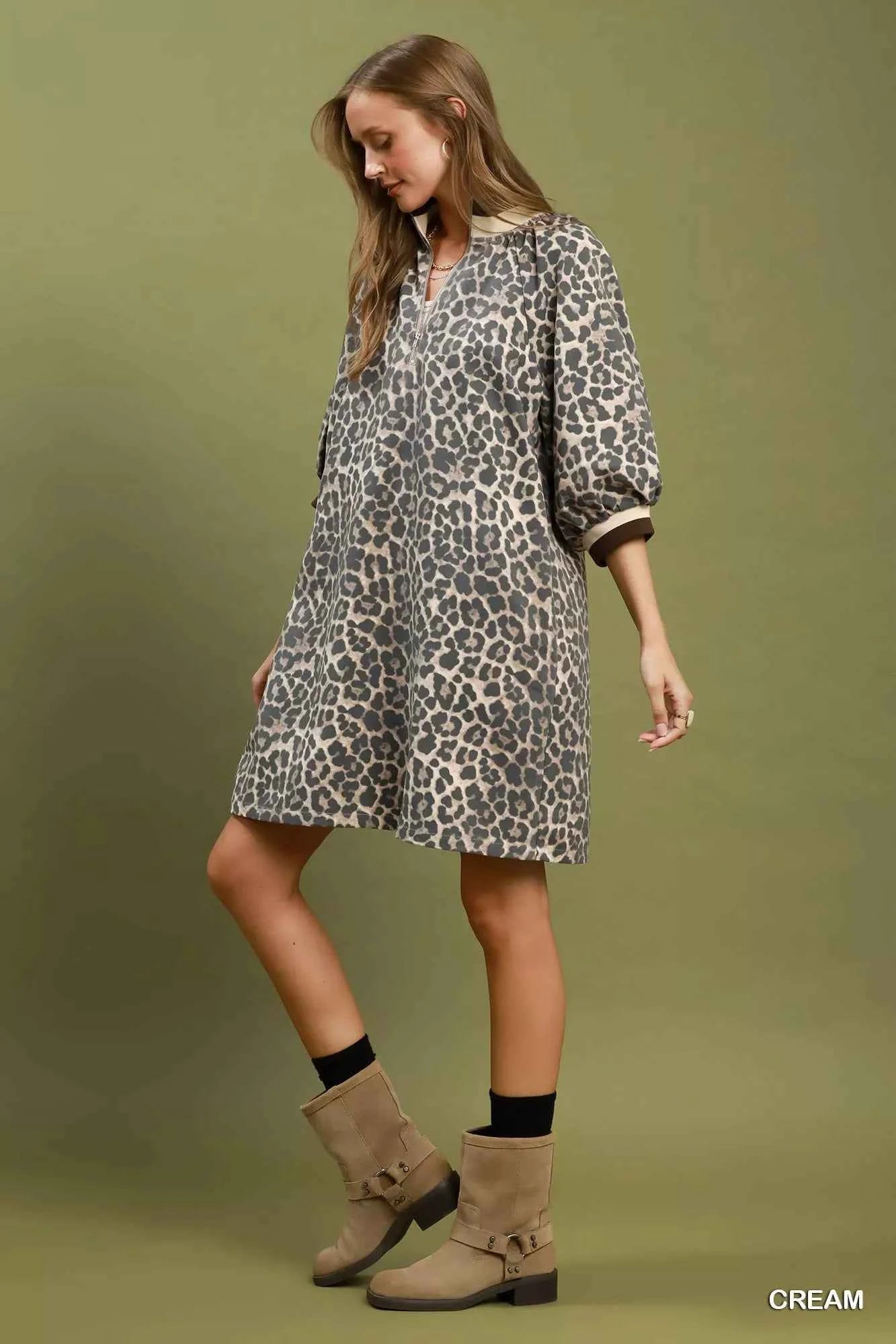 Woman wearing a cream leopard print mini dress by Umgee featuring a quarter-zip neckline, puff sleeves, contrast trim, relaxed fit, and side pockets. side view