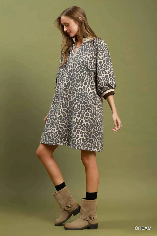Woman wearing a cream leopard print mini dress by Umgee featuring a quarter-zip neckline, puff sleeves, contrast trim, relaxed fit, and side pockets. side view