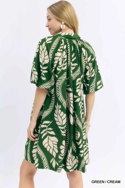 Woman wearing a green and cream leafy ogee print mini dress with a collared V-neckline and side pockets by Umgee. back view