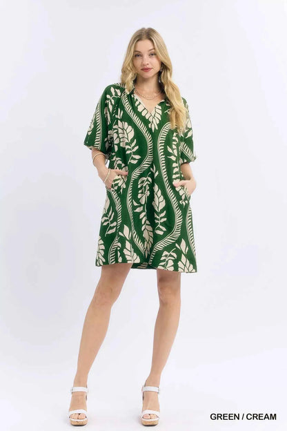 Woman wearing a green and cream leafy ogee print mini dress with a collared V-neckline and side pockets by Umgee. full view
