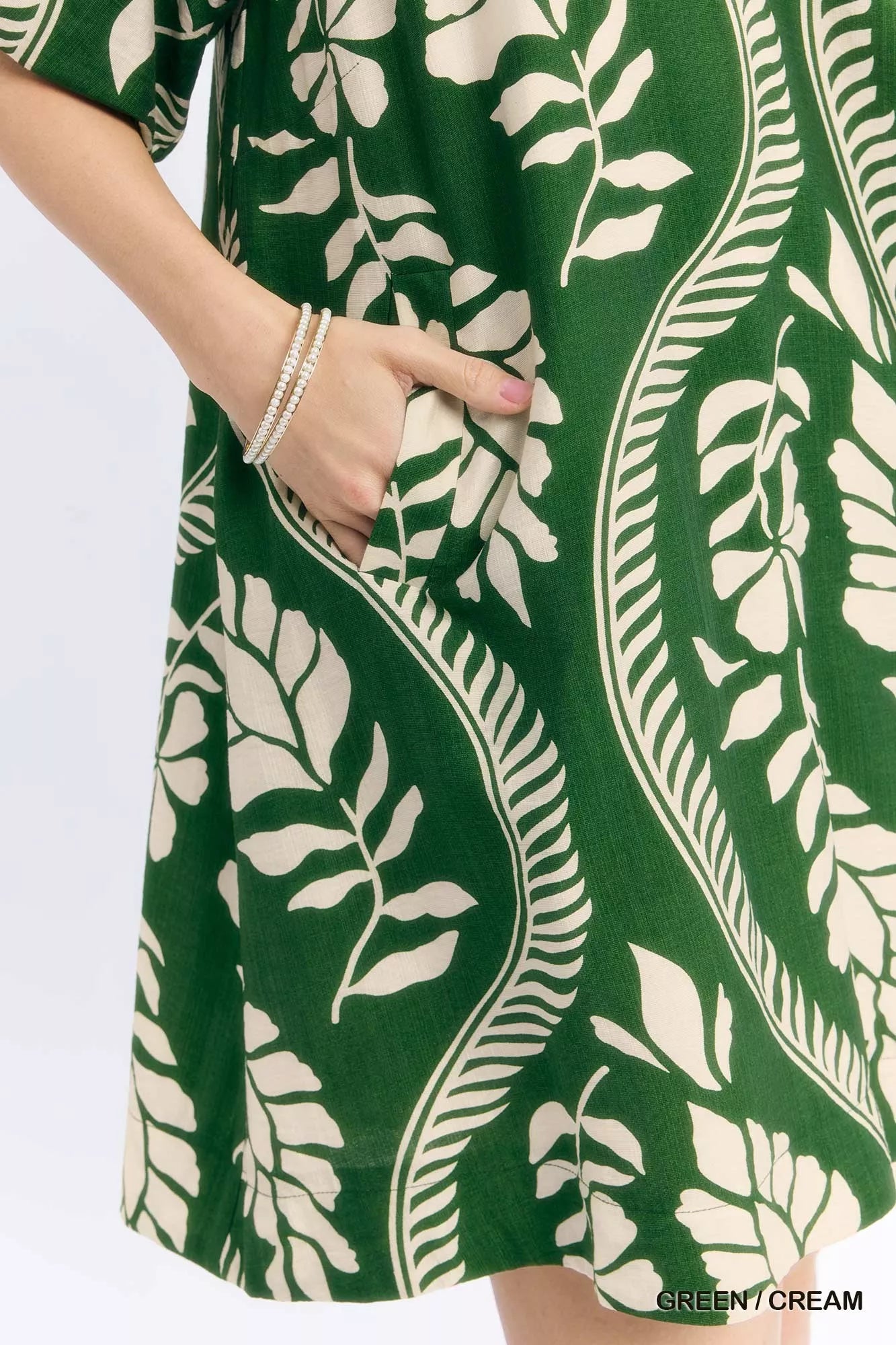 Woman wearing a green and cream leafy ogee print mini dress with a collared V-neckline and side pockets by Umgee. pocket view