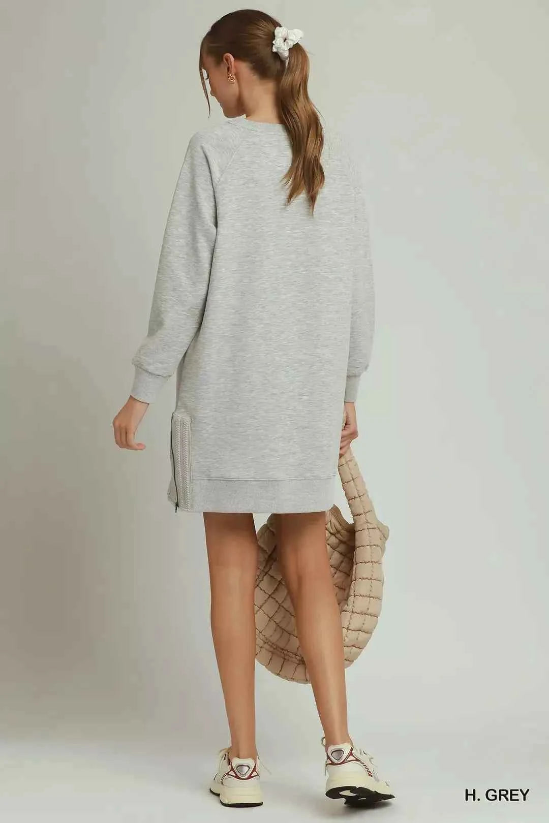Woman wearing a heather grey sweatshirt dress with side crochet trim, zipper details, pockets, and long sleeves by Umgee. Back View